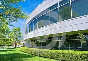 Green hedge and mowed lawn along round shaped wall of the office building