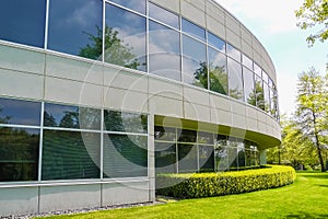 Green hedge and mowed lawn along round shaped wall of the office building