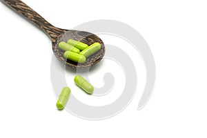 Green herbal capsules, medaical pills in wooden spoon on white.