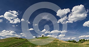 Green hill and a big blue sky with a few white clouds.