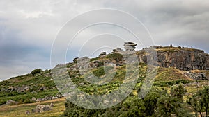 a green hill covered with rocks and shrubbery under cloudy skies