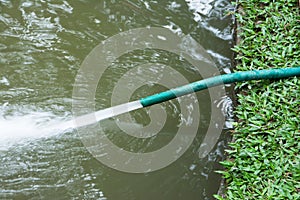 Green hose with water  drain spraying on the pond