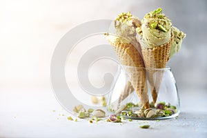 Green ice cream in waffle cone with chocolate and pistachio nuts on grey stone background. Summer food concept, copy