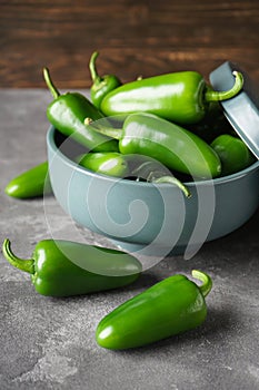 Green jalapeno peppers in a ceramic bowl on a gray background, close-up. Vertical