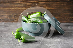 Green jalapeno peppers in a ceramic bowl on a gray wooden background