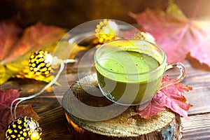 Green Japanese matcha tea with foam in transparent Cup on wooden table in autumn still life. Warm atmosphere and comfort, lights