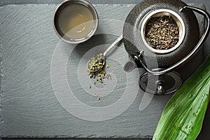 Green japanese tea on black slate. Black teapot with dry green tea. Tea preparation. Top view with copy space.