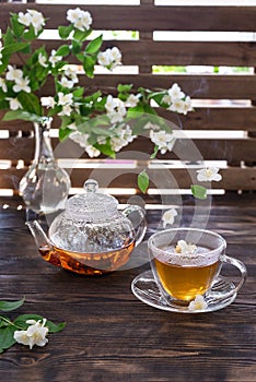 Green jasmine tea in transparent cup with hot steam and jasmine flowers and teapot on wooden table. Copy space. Food levitation