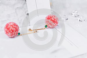 Green jeweled earrings with pink furry balls on them.Earrings are flanked by transparent ice cubes and other decorations