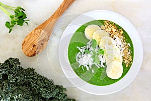 Green kale smoothie bowl overhead scene on white marble