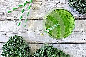 Green kale smoothie with straw overhead view on old wood