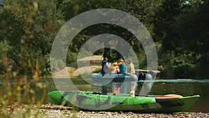 Green kayak on the river bank. In the background, a boat with people floats by. Real time. The concept of kayaking and