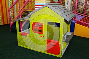 Green kids playhouse in the entertainment center. Plastic children play house with red and orange door and window. Green floor.