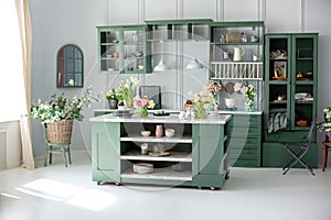 Green kitchen interior with furniture. Stylish cuisine with flowers in vase. Wooden kitchen in spring decor. Cozy home decor. Kitc