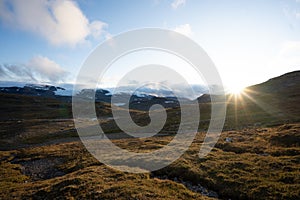 Green land surrounded by high rocky mountains with the bright sun in the background in Finse, Norway