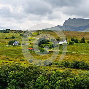 Green landscape with high mountains and cottages on the Isle of Skye, Scotland, UK.