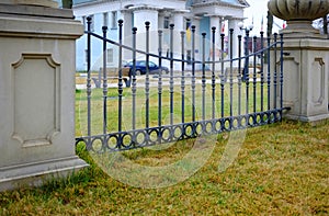 Green lawn in front of a decorative fence with bars, background. Beautiful wrought fence. Image of a decorative cast iron fence