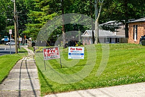 A green lawn in front of a house with two for sale signs on a sunny day