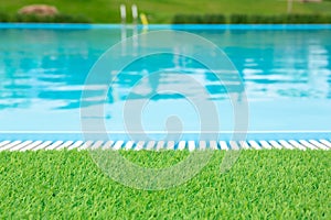 green lawn grass on the background of a pool with clear blue water