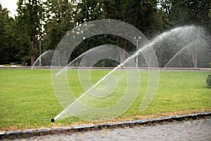 On green lawn, in a park or garden, a sprinkler is working. Automatic sprinkler irrigation system or device for watering of lawn.