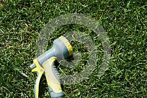 On the green lawn there is a hose for watering plants. A water hose with a sprayer for watering plants in the garden