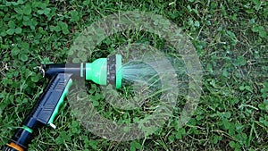 On the green lawn there is a hose for watering plants. A water hose with a sprayer for watering plants in the garden