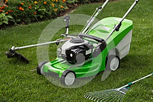 Green lawnmower, weed trimmer, rake and secateurs in the garden