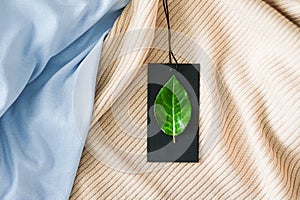 Green leaf on clothing tag and organic fabric background, sustainable fashion and brand label concept