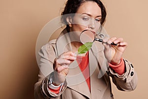 A green leaf in the hands of a woman examaing the structure of the plant through a loupe, on isolated background