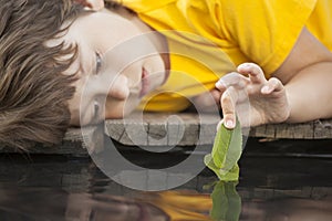 Green leaf-ship in children hand in water, boy in park play with