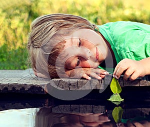 Green leaf-ship in children hand in water, boy in park play with boat in river