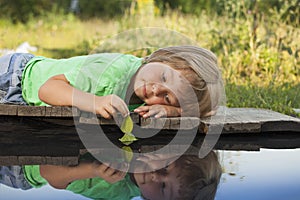 Green leaf-ship in children hand in water, boy in park play with boat in river