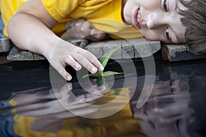 Green leaf-ship in children hand in water, boy in park play with boat in river