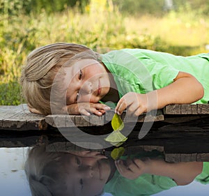 Green leaf-ship in children hand in water, boy in park play with boat in river