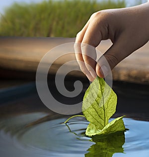 Green leaf-ship in children hand in water. Boy in park play with boat in river