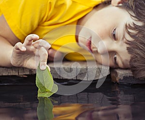 green leaf-ship in children hand in water, boy in park play with boat in river