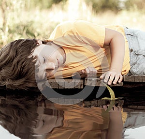 Green leaf-ship in children hand in water, boy in park play with boat in river