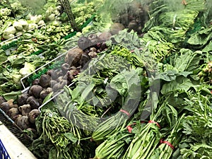 Green leafy vegetables and root crops at the fresh produce section in a grocery store