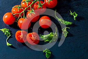 Green leaves of kale sprouts and fresh vine tomatoes cherry with drops of water, raw, whole and halved. On black textured slate