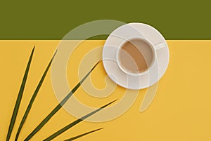 Green leaves, white cup of coffee, yellow, green background. Place for text. Flat lay. Top view. Copy space