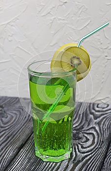 Green lemonade in a glass. Garnished with a slice of lemon and kiwi. With a straw for a cocktail