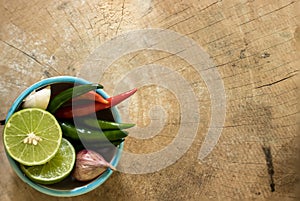 Green lemons, garlic, shallots and fresh chilli in a cup placed on a wooden