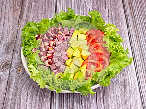 Green lettuce salad with fresh mixed purple corn, purple yams, avocado, and tomatoes on wooden table background.