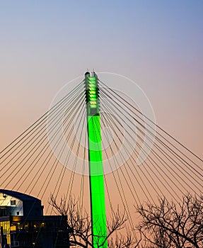 Green lighting of tower and cables of Bob Kerrey foot bridge with backdrop of River Front Condominiums Omaha Nebraska