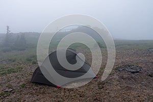 Green lightweight freestanding three-season 2-person tent on  hill in grass in the evening after rainstorm.  Jesenik mountains,