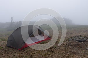 Green lightweight freestanding three-season 2-person tent on  hill in grass in the morning after rainstorm.  Jesenik mountains,