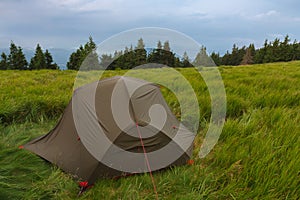 Green lightweight freestanding three-season 2-person tent on mravenecnik hill in grass in the morning after rainstorm