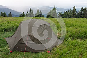 Green lightweight freestanding three-season 2-person tent on mravenecnik hill in grass in the morning after rainstorm