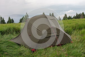 Green lightweight freestanding three-season 2-person tent on mravenecnik hill in grass in the morning after rainstorm