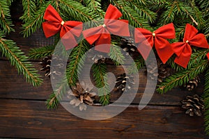 Green living spruce branches on a dark wooden background. New Year background with cones and red bows. Top view